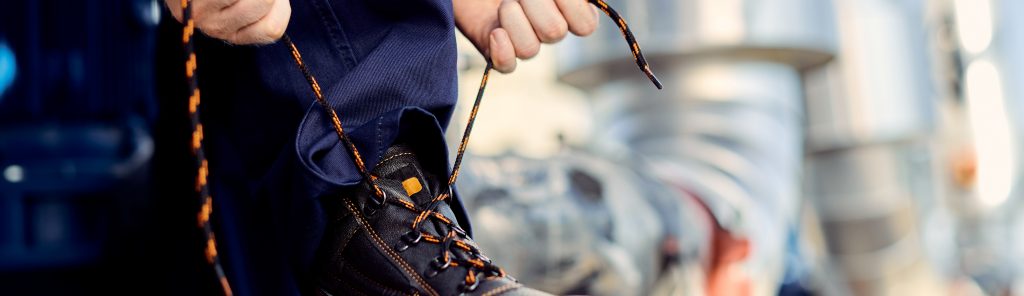 Unrecognizable construction worker tying his shoelace outdoors.